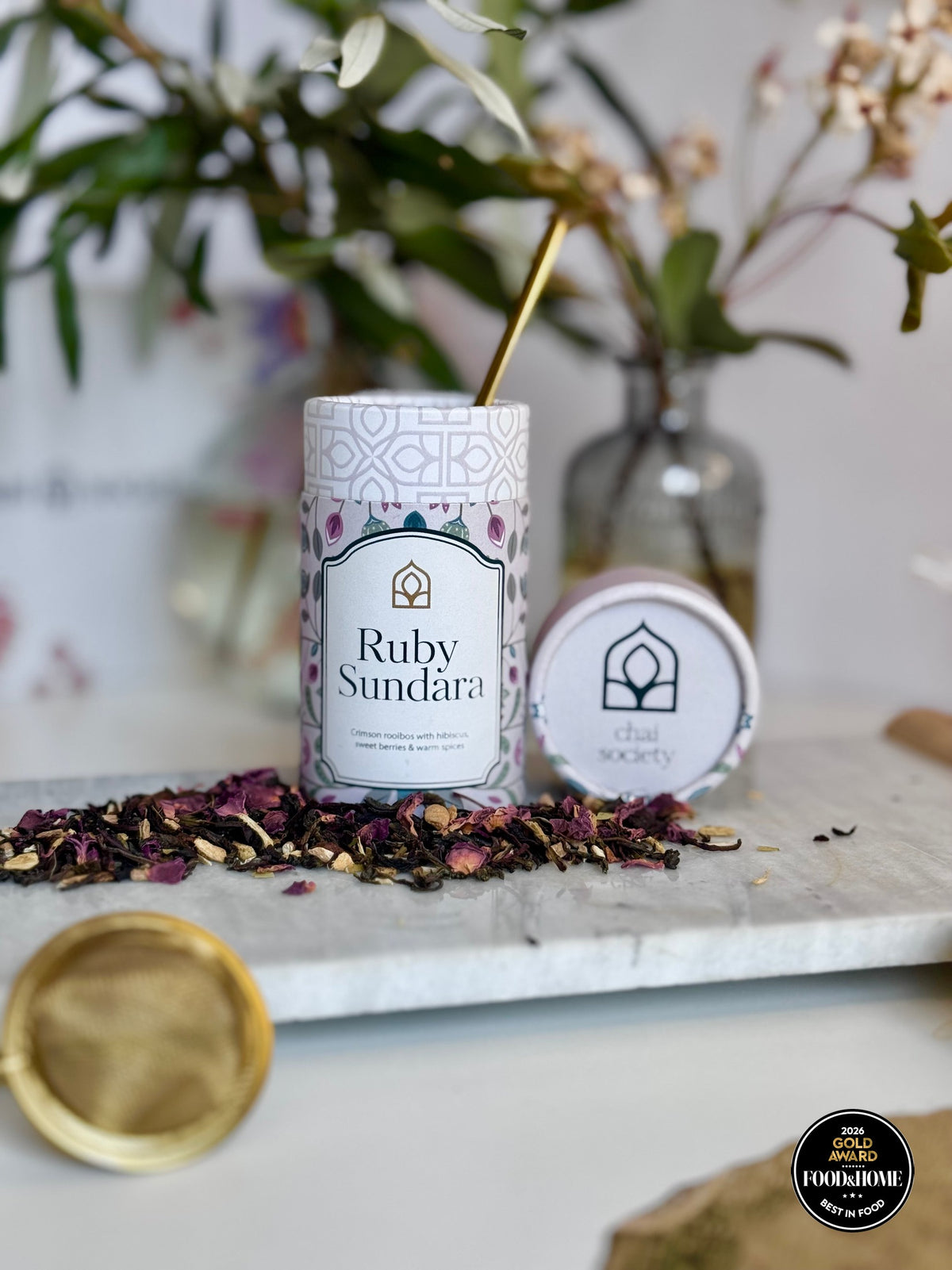 Ruby Sundara rooibos canister with loose tea leaves and a gold strainer