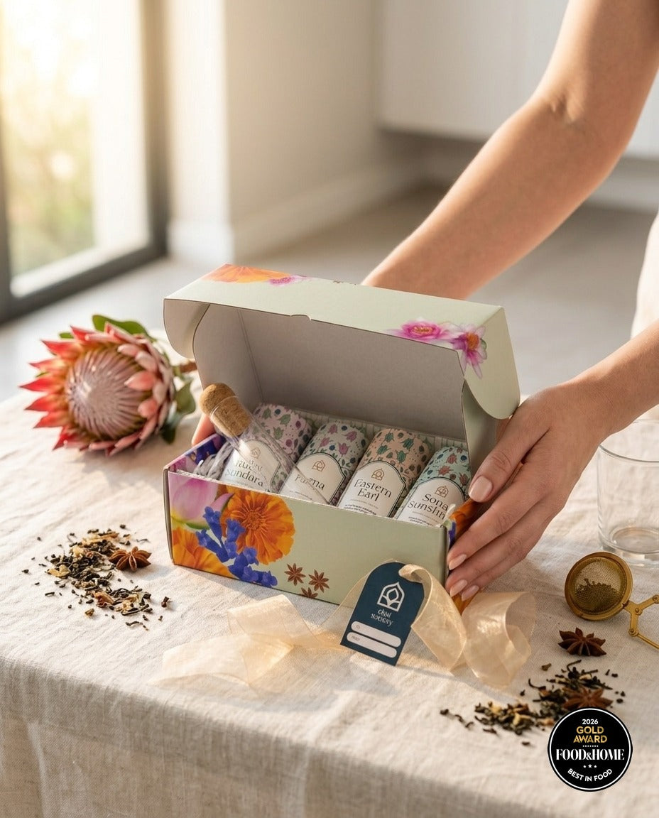 Opening a Chai Society tea gift box on a linen-covered table beside a protea