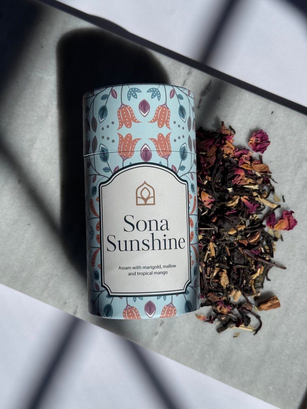 Tea canister labeled 'Sona Sunshine' with dried tea leaves on a light surface